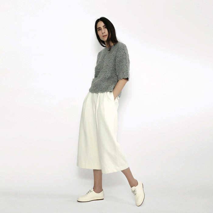 Woman wearing cropped off-white wide legged trousers.