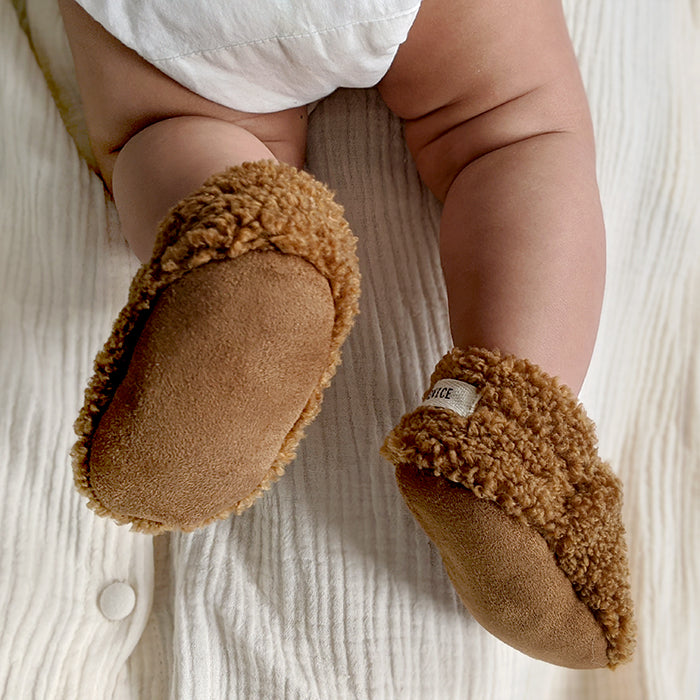 Baby being held wearing a pair of brown faux shearling baby booties.