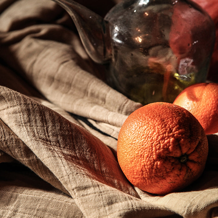 Beige cotton gauze tablecloth on a table with some orange.