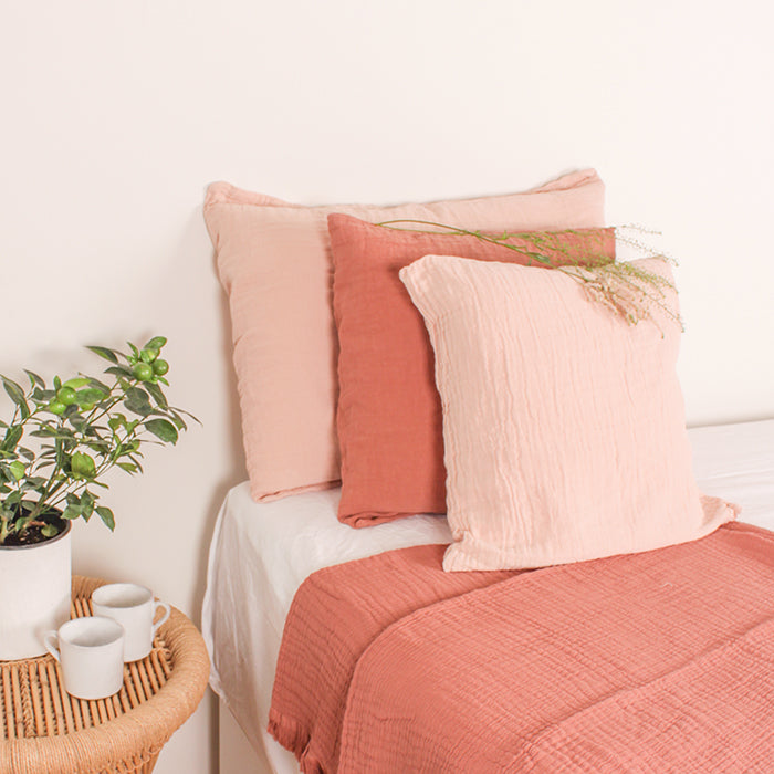 A stack of pink and red pillows on a bed.
