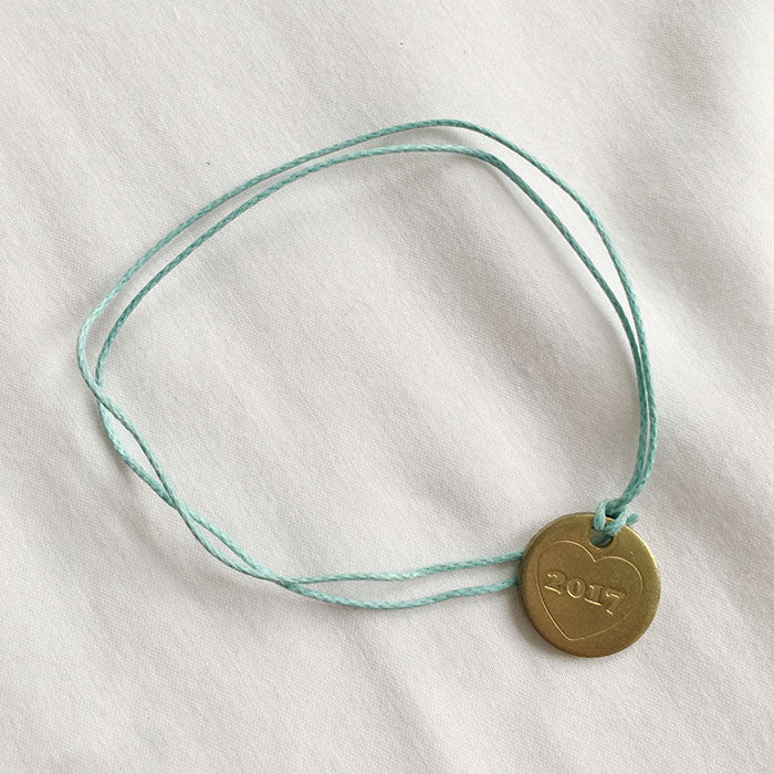 Brass medallion with "2017" embossed on it on a blue string bracelet.