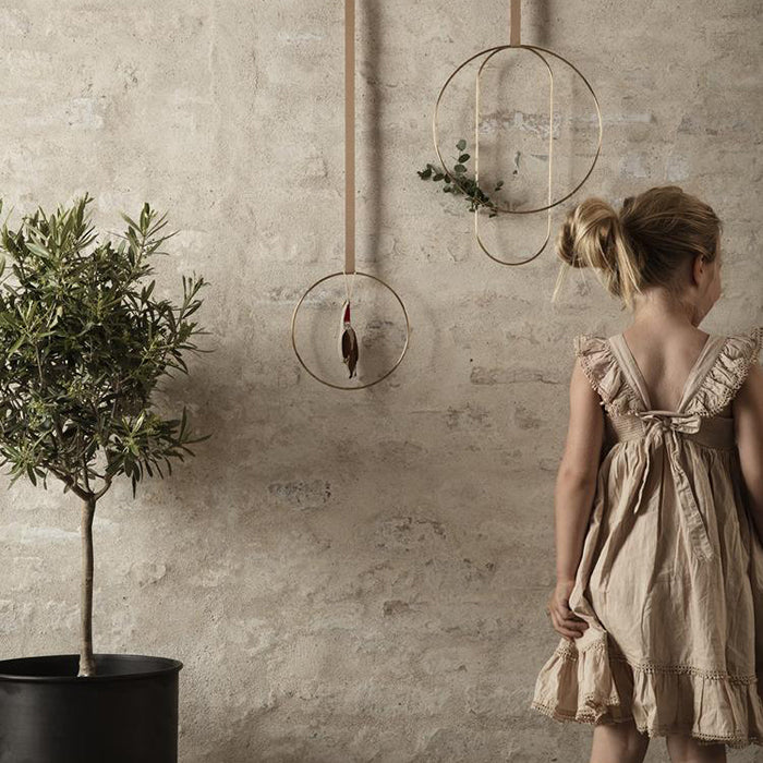 Girl standing next to gold coloured brass rings in three shapes and sizes hanging on a brick wall.