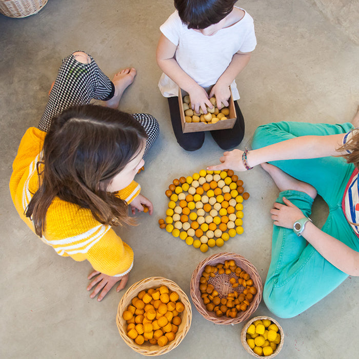 Children playing with wooden mini honeycomb shaped pieces in various shades of yellow in a bowls.