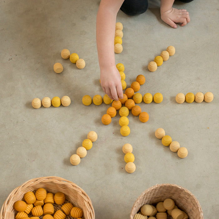 Child playing with wooden mini honeycomb shaped pieces in various shades of yellow in a star pattern.