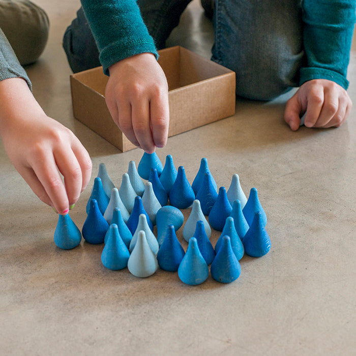 Child playing with wooden mini raindrop shaped pieces in various shades of blue.