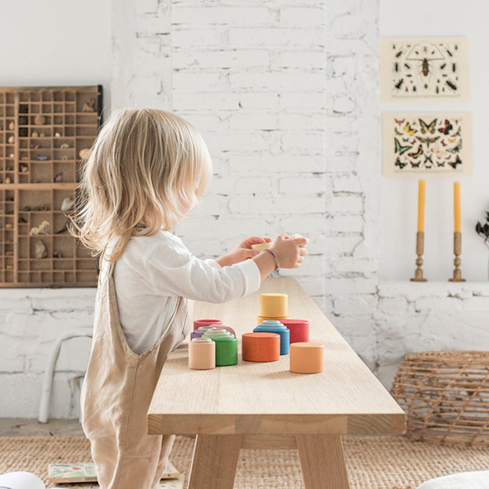 Child playing with nesting bowls in rainbow colours on a table.