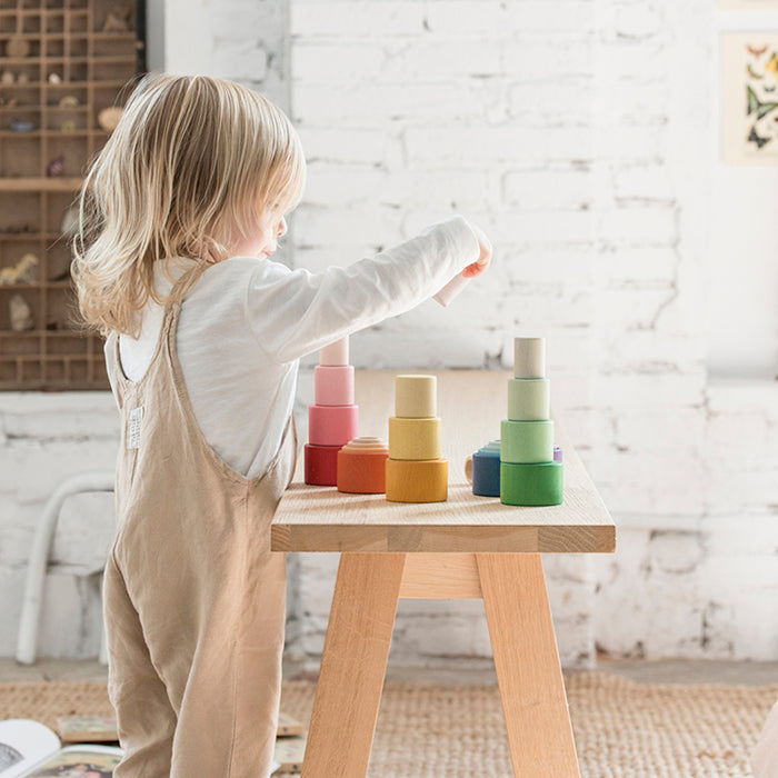 Child playing with nesting bowls in rainbow colours on a table.