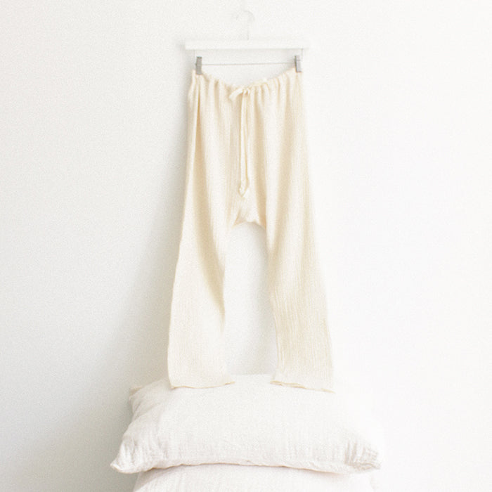 Cream muslin pants hanging above a stack of pillows.