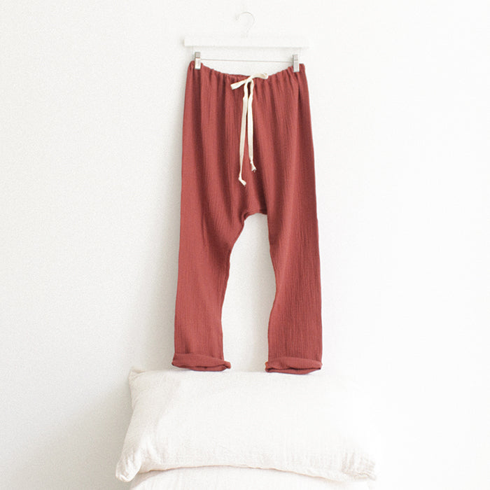 Red brown muslin pants with cuffed hems hanging above a stack of pillows.