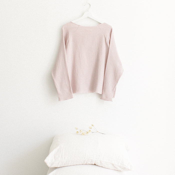 Red brown muslin shirt with long sleeves from the back hanging above a stack of pillows.