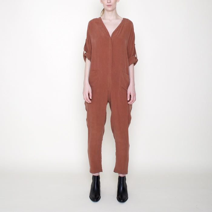 Woman wearing a rust red long sleeved jumpsuit with long legs and buttons from the front.