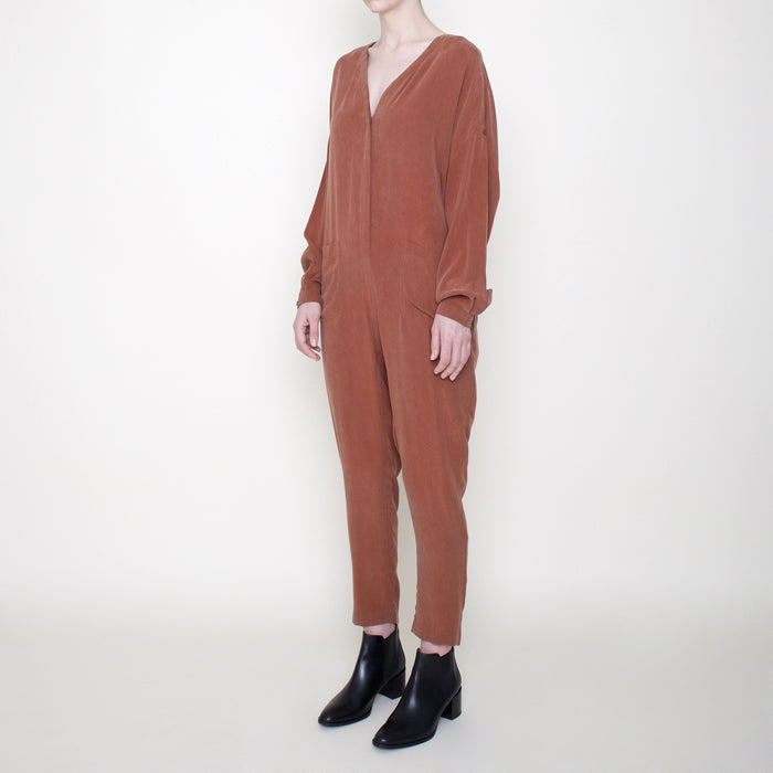 Woman wearing a rust red long sleeved jumpsuit with long legs and buttons from the side.