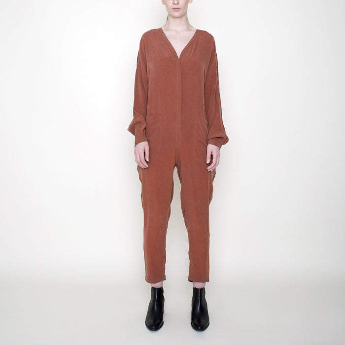 Woman wearing a rust red long sleeved jumpsuit with long legs and buttons from the front.
