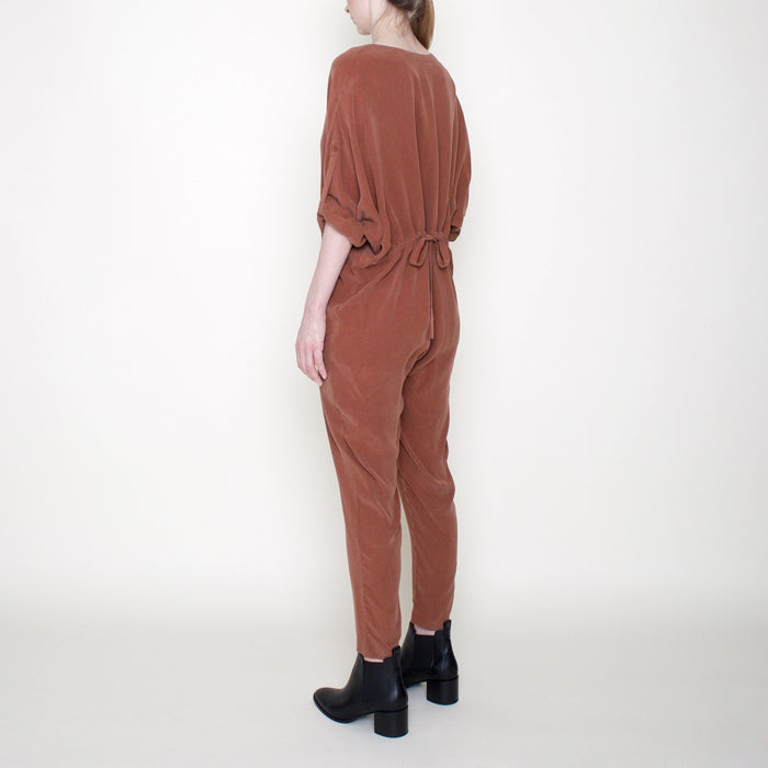 Woman wearing a rust red long sleeved jumpsuit with long legs and buttons from the back side.