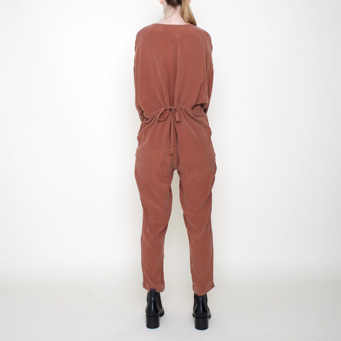 Woman wearing a rust red long sleeved jumpsuit with long legs and buttons from the back.