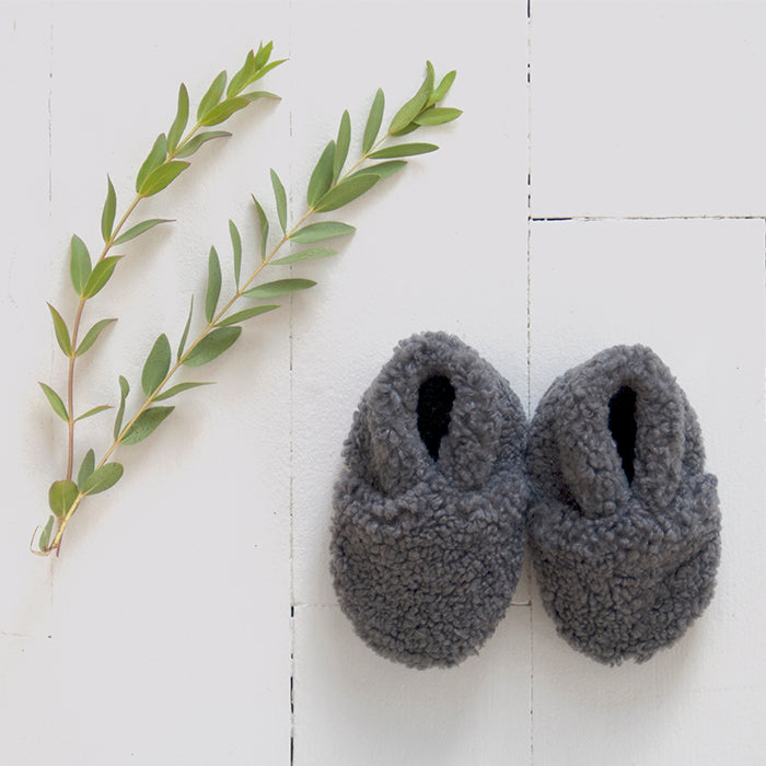 Pair of grey faux shearling baby booties next to some leaves.