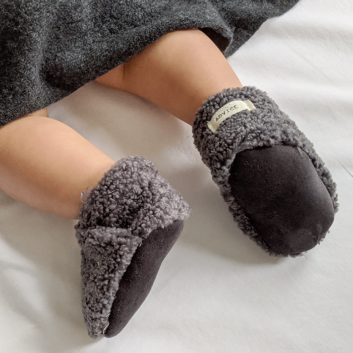Baby laying down wearing a pair of grey faux shearling baby booties.