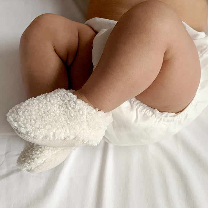 Baby laying down wearing a pair of cream faux shearling baby booties.