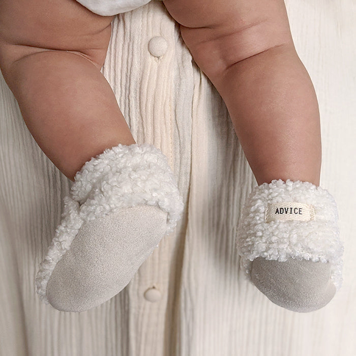 Baby being held wearing a pair of cream faux shearling baby booties.