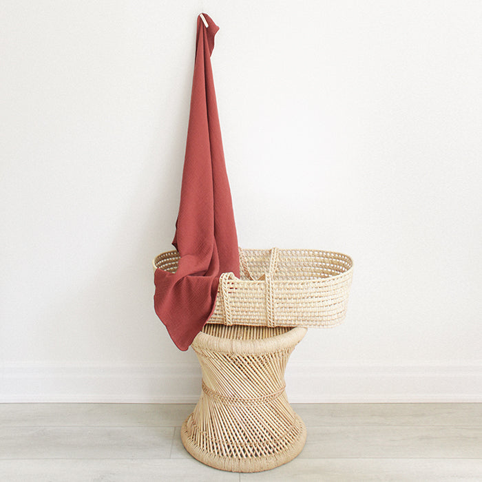 Red brown muslin baby blanket hanging above a bassinet.