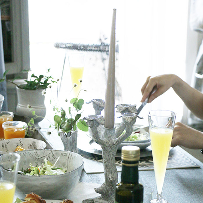 Tree shaped candlestick holder on a dinner table with a long taper candle held in the middle.
