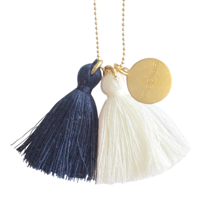 Brass chain necklace with blue and cream tassels and a brass charm with the word "imagine" on it.