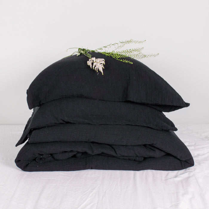 Black duvet and pillows stacked on a bed with some fresh flowers on top.