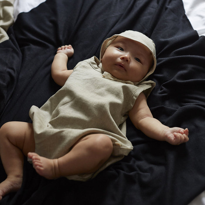 Baby wearing a matching cream newborn outfit with a bonnet and sleeveless romper with no legs.