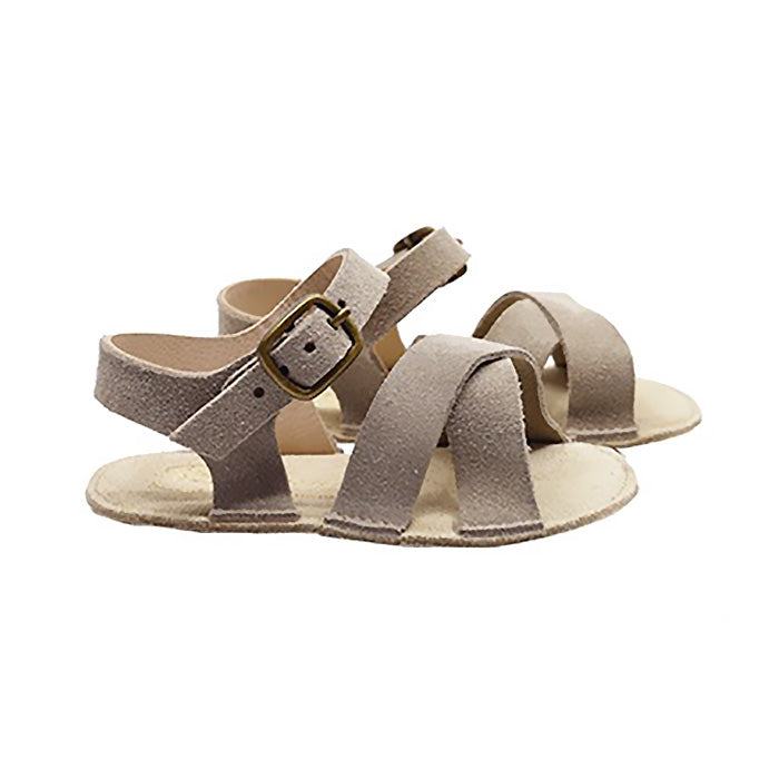 A pair of grey brown sandals with a buckle around the ankle from the side.