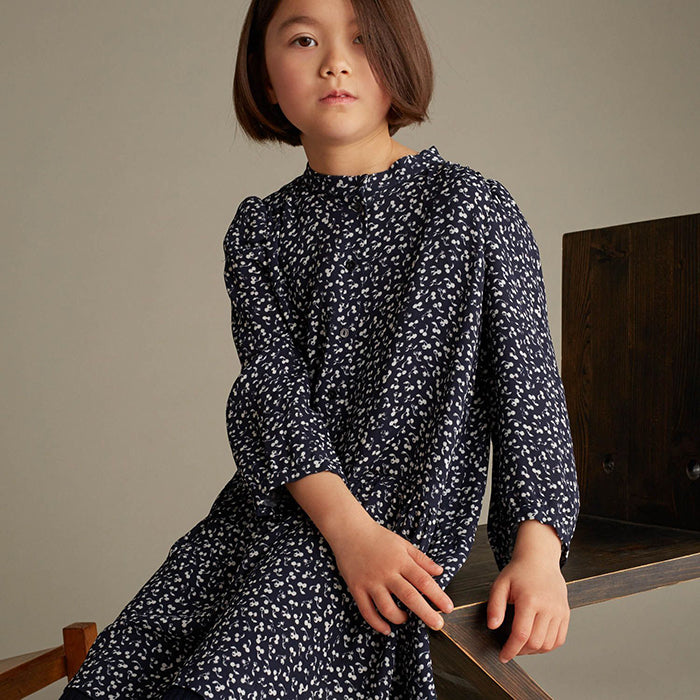 Girl sitting wearing a long sleeved dress in navy with an all over white cherry print.