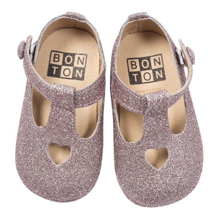 A pair of mary jane shoes with a heart cutout in pink and silver glitter from the top.