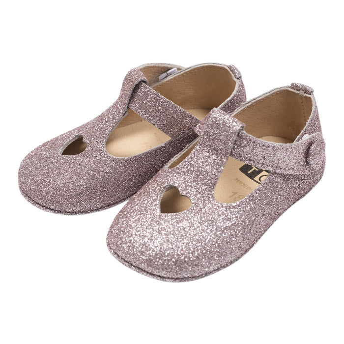 A pair of mary jane shoes with a heart cutout in pink and silver glitter from the side.