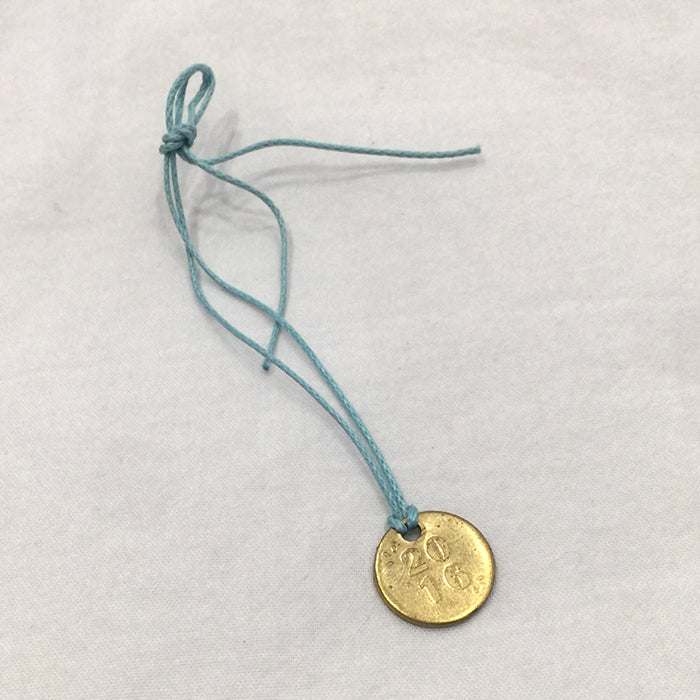 Brass medallion with "2016" embossed on it on a blue string bracelet.