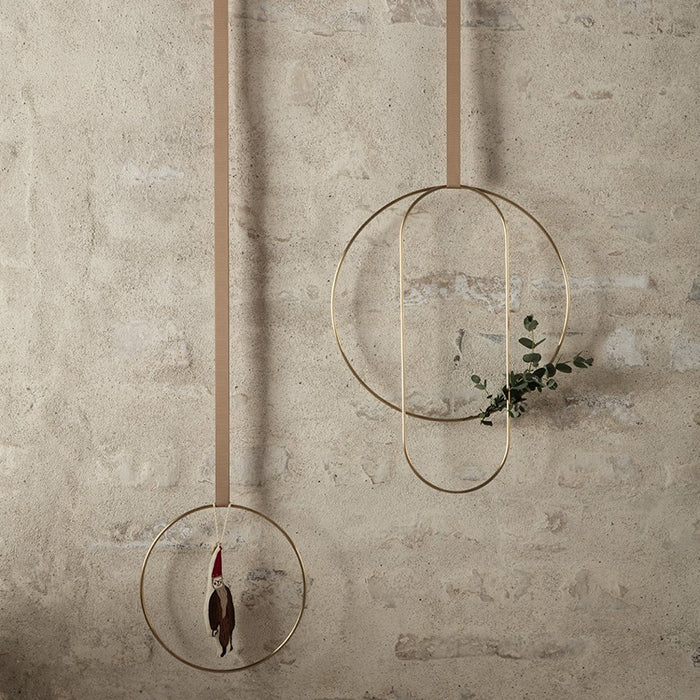 Gold coloured brass rings in three shapes and sizes hanging on a brick wall.