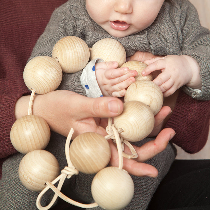 Baby being held playing with a string of round wooden beads.