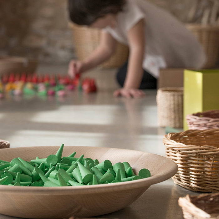 Wooden mini cone shaped pieces in various shades of green in a wooden bowl.