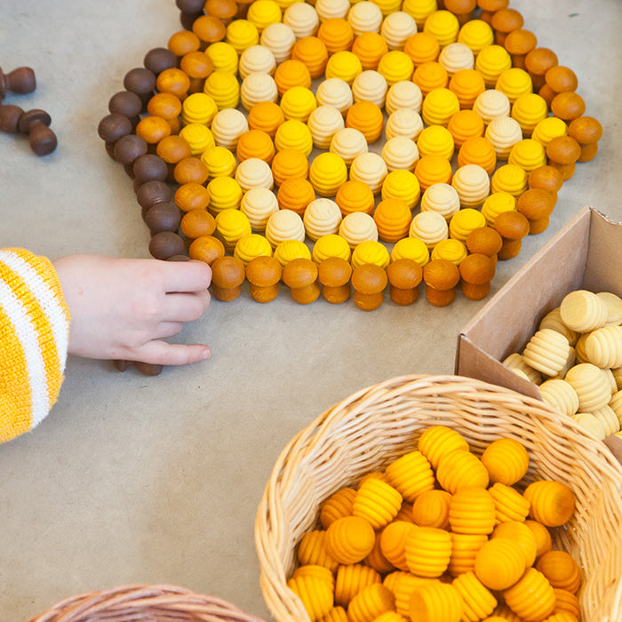 Child playing with wooden mini honeycomb shaped pieces in various shades of yellow.