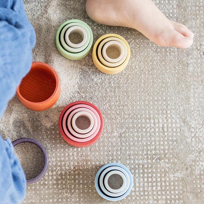 Child playing with nesting bowls in rainbow colours.