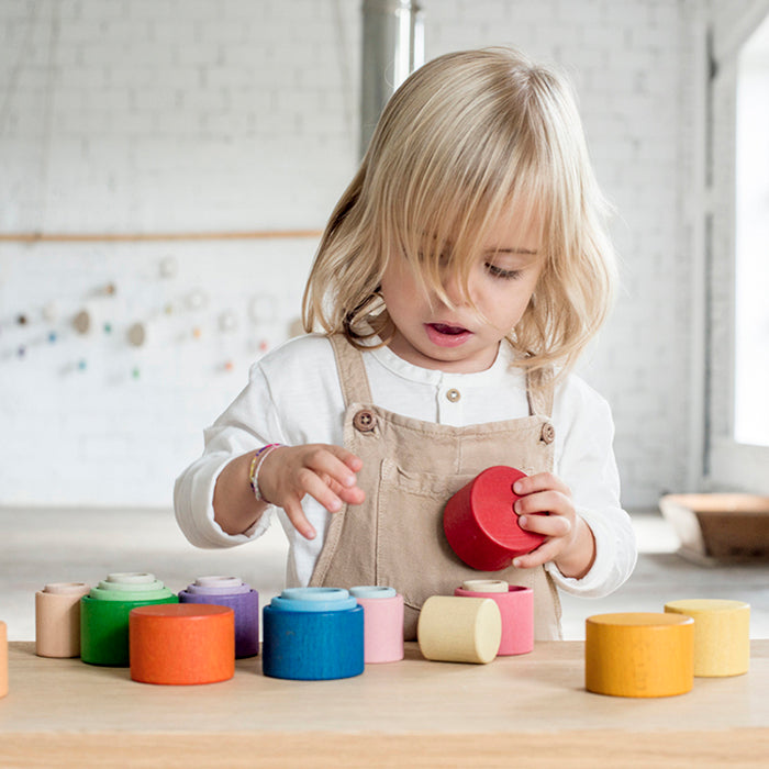 Child playing with nesting bowls in rainbow colours.