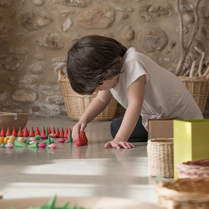 Boy playing with wooden mini teardrop shaped pieces in various shades of red and orange.