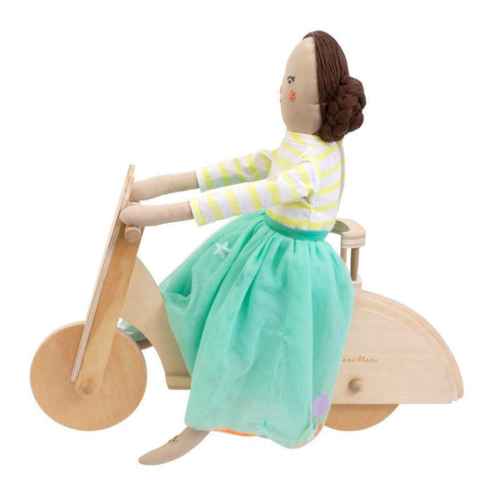 Doll sitting on a wooden moped from the side.