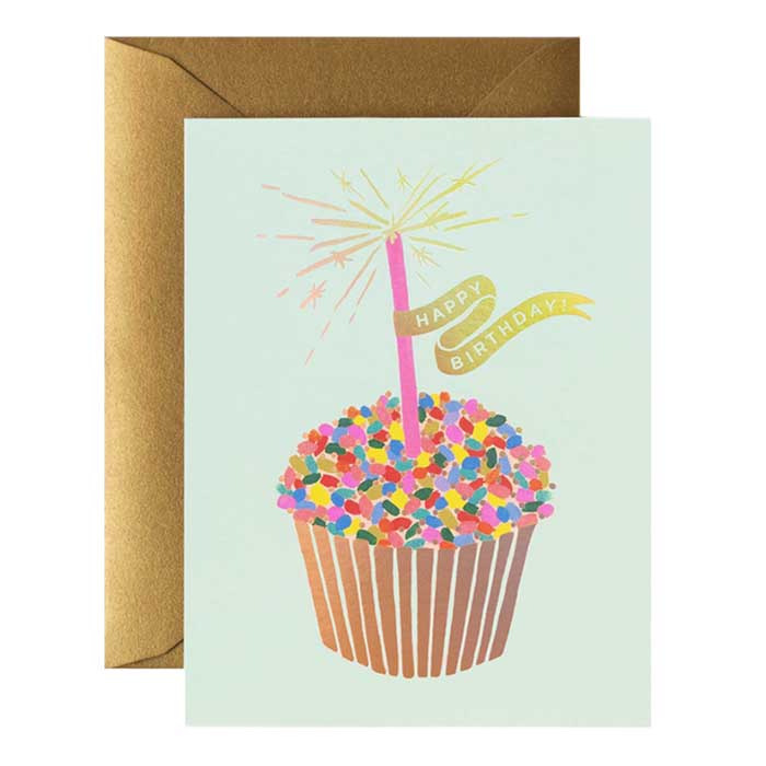 A birthday card with a multicoloured cupcake print over a gold envelope.
