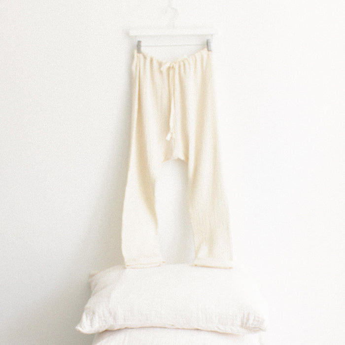 Cream muslin pants with cuffed hems hanging above a stack of pillows.