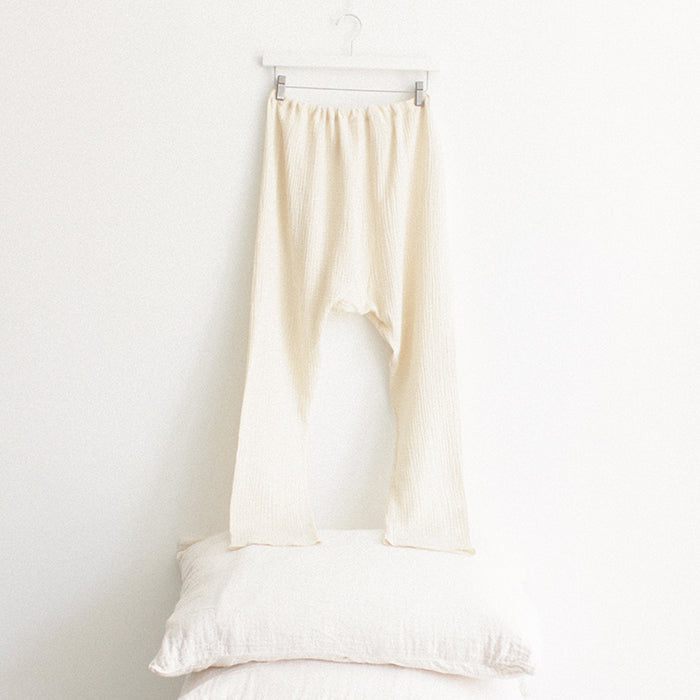 Cream muslin pants from the back hanging above a stack of pillows.