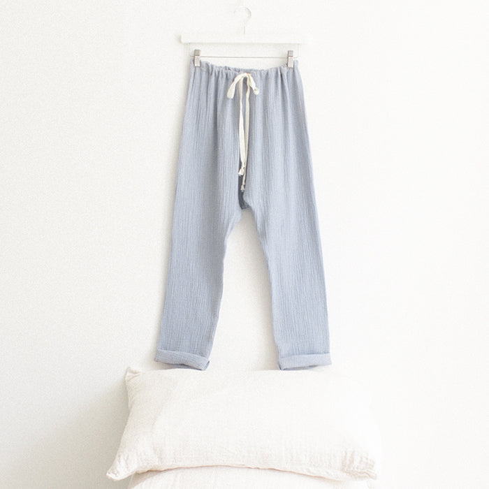 Light blue muslin pants with cuffed hems hanging above a stack of pillows.
