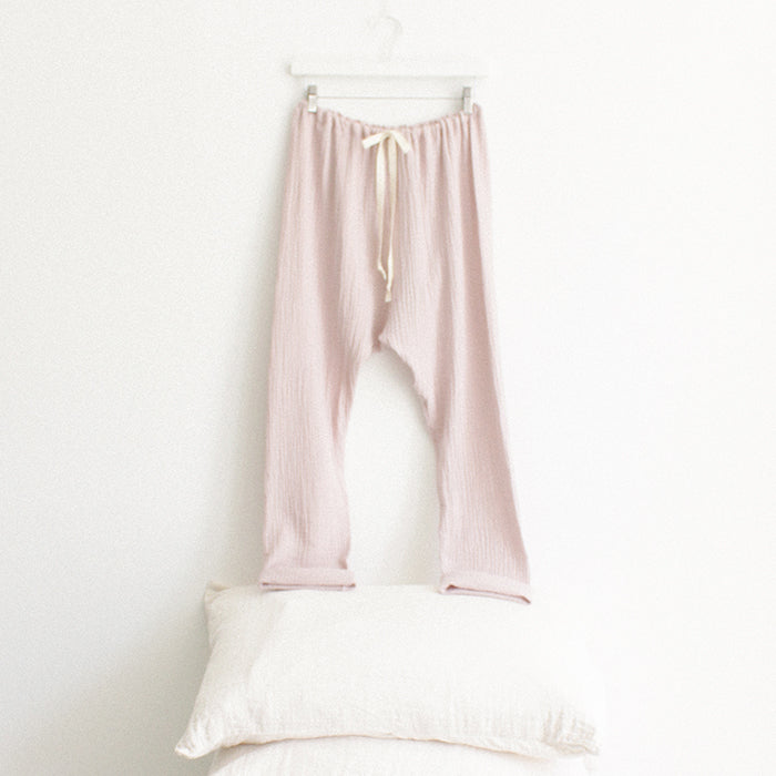 Light pink muslin pants with cuffed hems hanging above a stack of pillows.