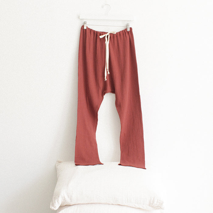 Red brown muslin pants hanging above a stack of pillows.