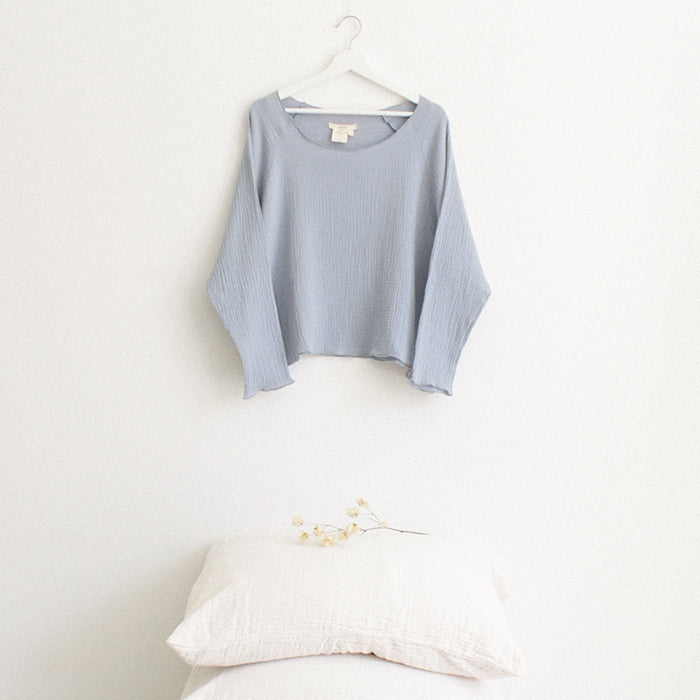 Light blue muslin shirt with long sleeves hanging above a stack of pillows.