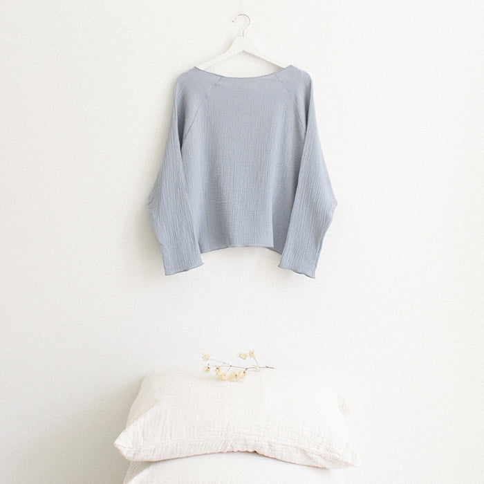 Light blue muslin shirt with long sleeves from the back hanging above a stack of pillows.
