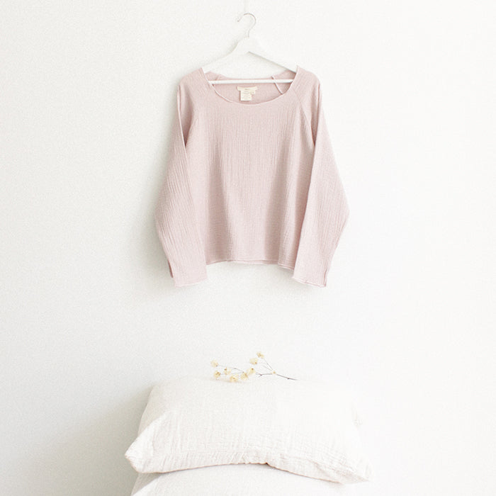 Light pink muslin shirt with long sleeves hanging above a stack of pillows.